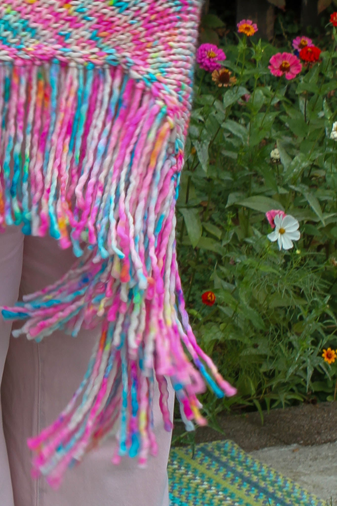 Colorful woven blanket with fringe against a natural background with flowers fringe that flutters like petals in the wind