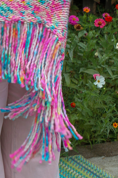 Colorful woven blanket with fringe against a natural background with flowers fringe that flutters like petals in the wind